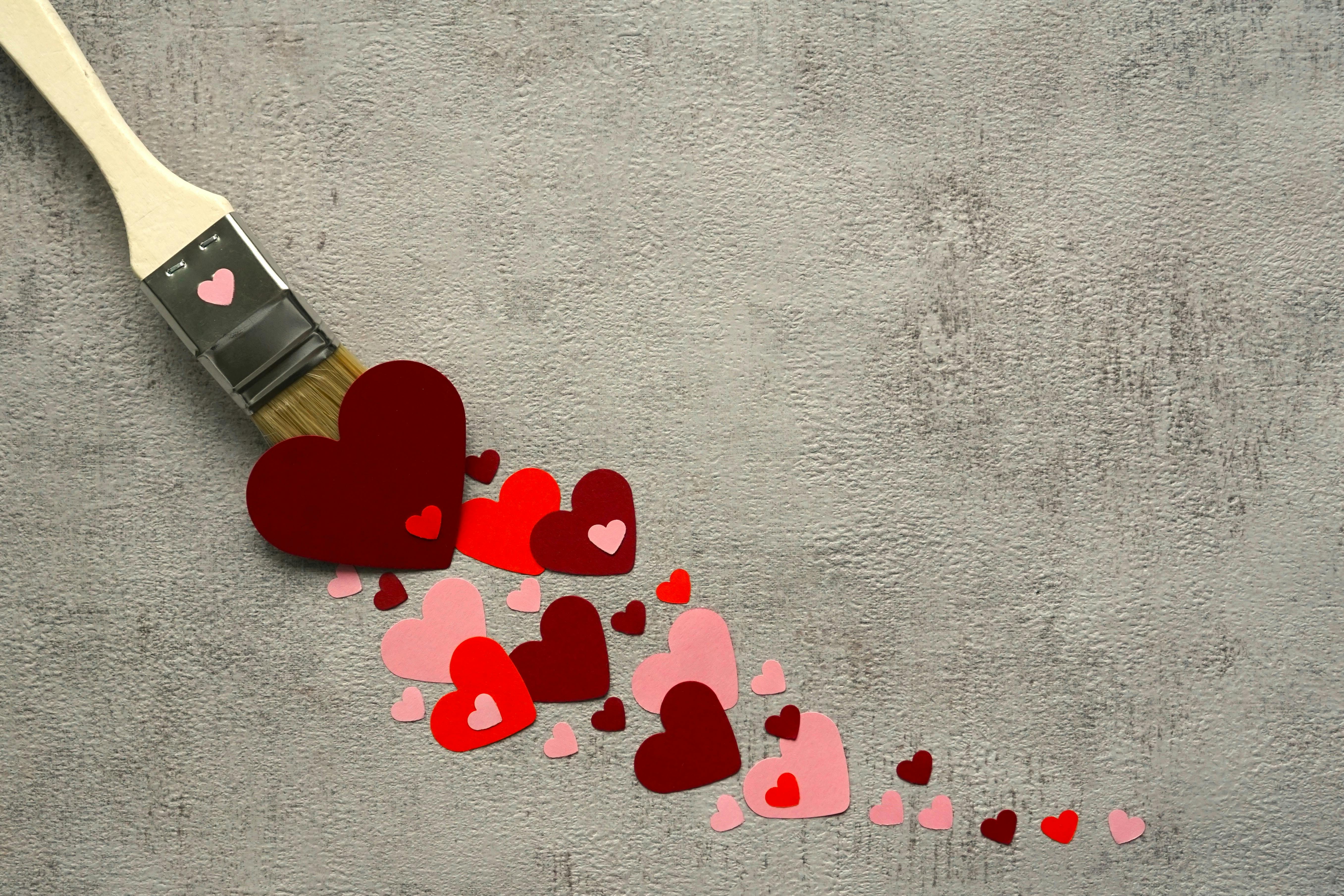 A paintbrush paints heart-shaped cutouts on a textured wall, symbolizing creativity and love.