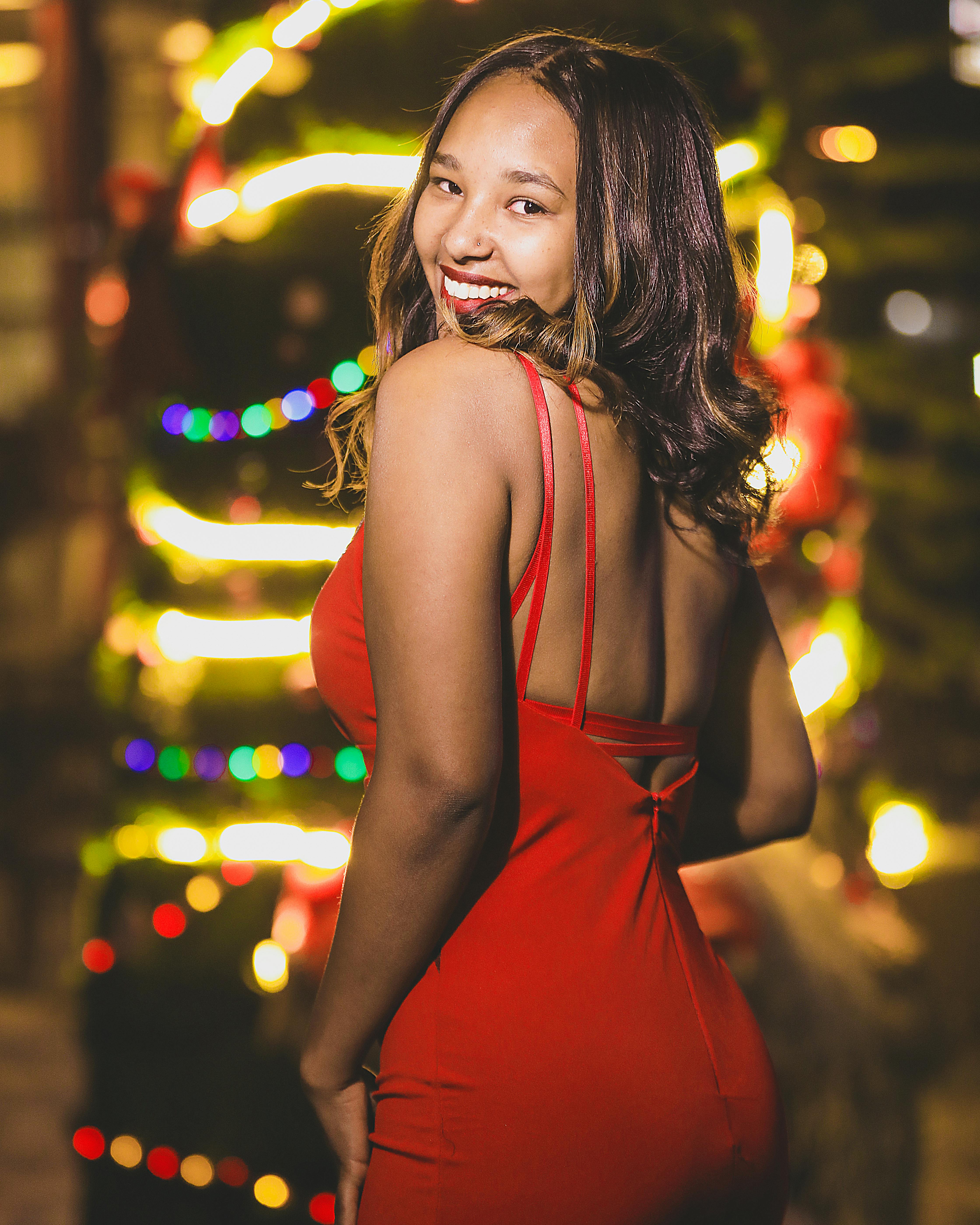 Stunning woman in a red dress posing gracefully against a colorful, festive bokeh background.