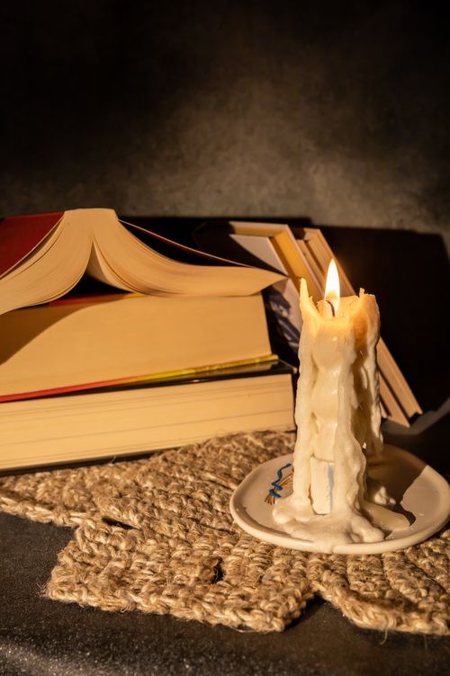 Free Warm, intimate scene with a candle and open books on woven mat. Ideal for reading themes. Stock Photo