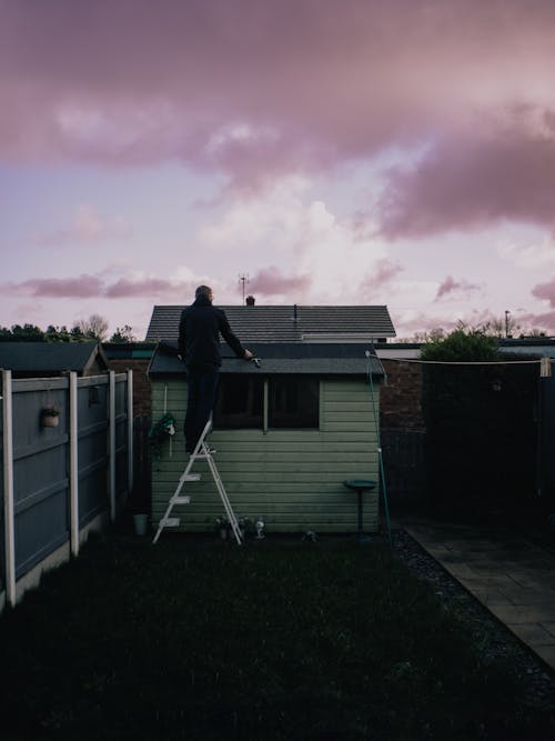 Man Standing on the Ladder in a Yard Fixing a Roof on a House 