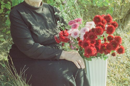 Woman Sitting next to a Bunch of Flowers in a Vase 