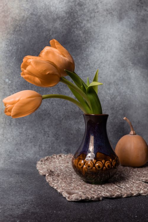 Free Close-up of vibrant orange tulips in a decorative vase with a soft background. Stock Photo