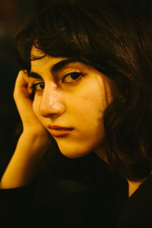 Free Close-up portrait of a young woman with brunette hair, resting her hand on her cheek, in soft lighting. Stock Photo
