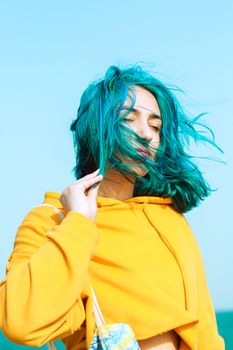Stylish young woman with vibrant blue hair enjoying a breezy day outdoors.
