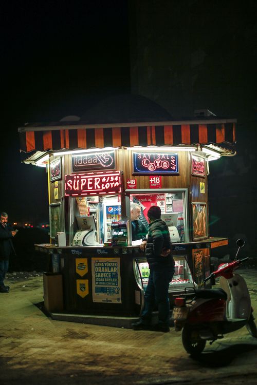 Free Illuminated urban scene of a newsstand at night with a motor scooter parked nearby, evoking city life. Stock Photo