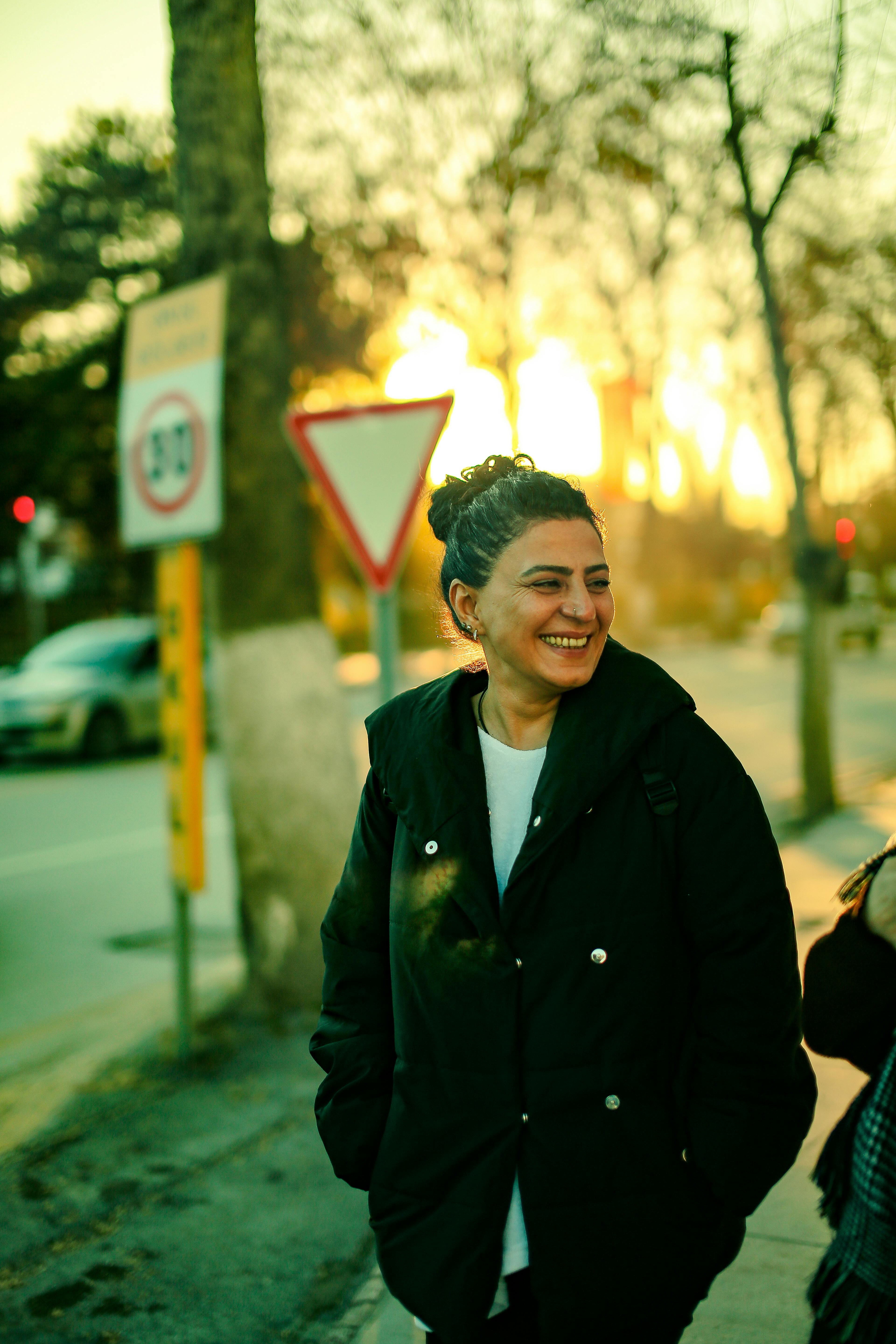 A woman smiles while standing outside during a colorful sunset in an urban setting.