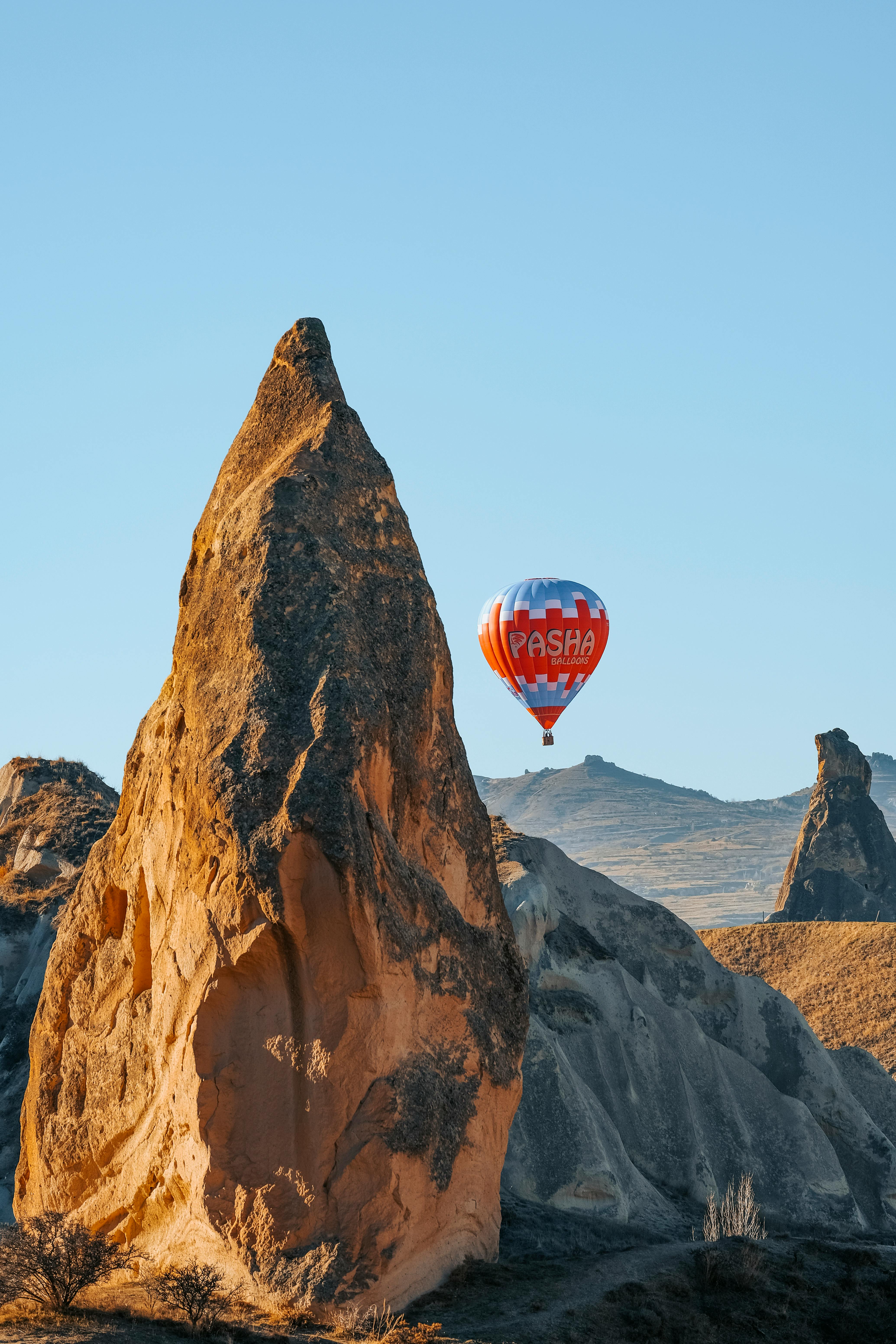 Hot air balloon flying over the unique rock formations of Cappadocia under clear blue skies.