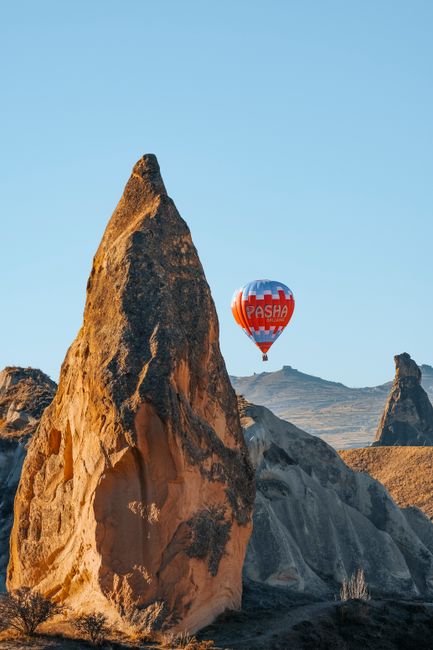 Hot air balloon flying over the unique rock formations of Cappadocia under clear blue skies.