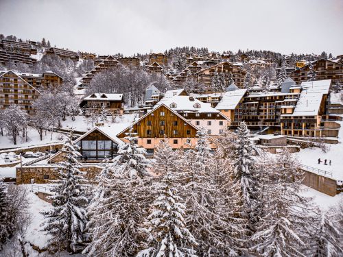 Free A picturesque aerial of a snow-covered mountain village surrounded by evergreen trees and buildings in winter. Stock Photo
