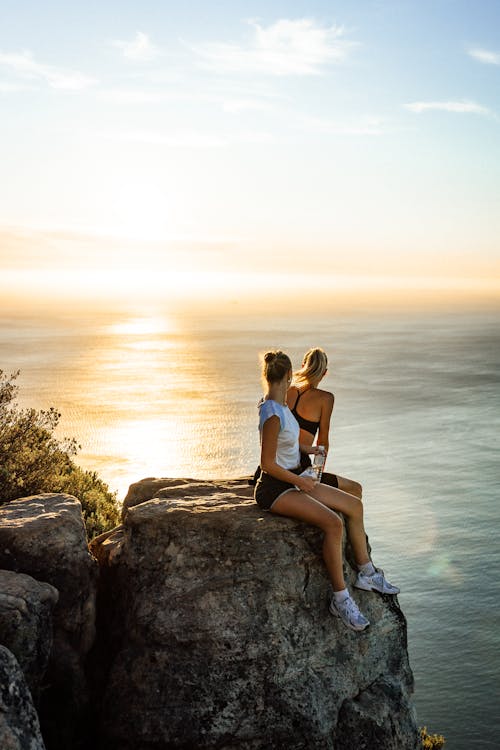 Young Women Sitting on a Seaside Cliff Looking at the Sunset