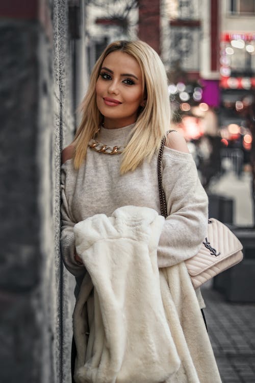 Young Woman Standing against a Wall of a Building in City and Smiling