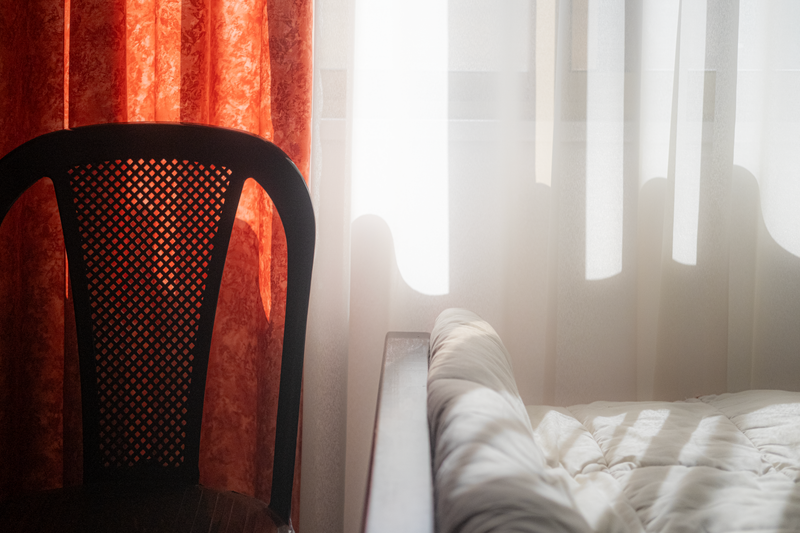 Sunlight streaming through curtains illuminating a bed and chair in a cozy bedroom setting.