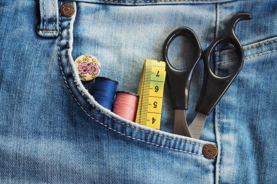 Close-up of sewing accessories in a denim pocket, featuring threads, scissors, and measuring tape.