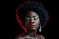 这幅优雅的肖像画描绘了一位留着非洲发型、画着鲜艳眼影和红唇的女性