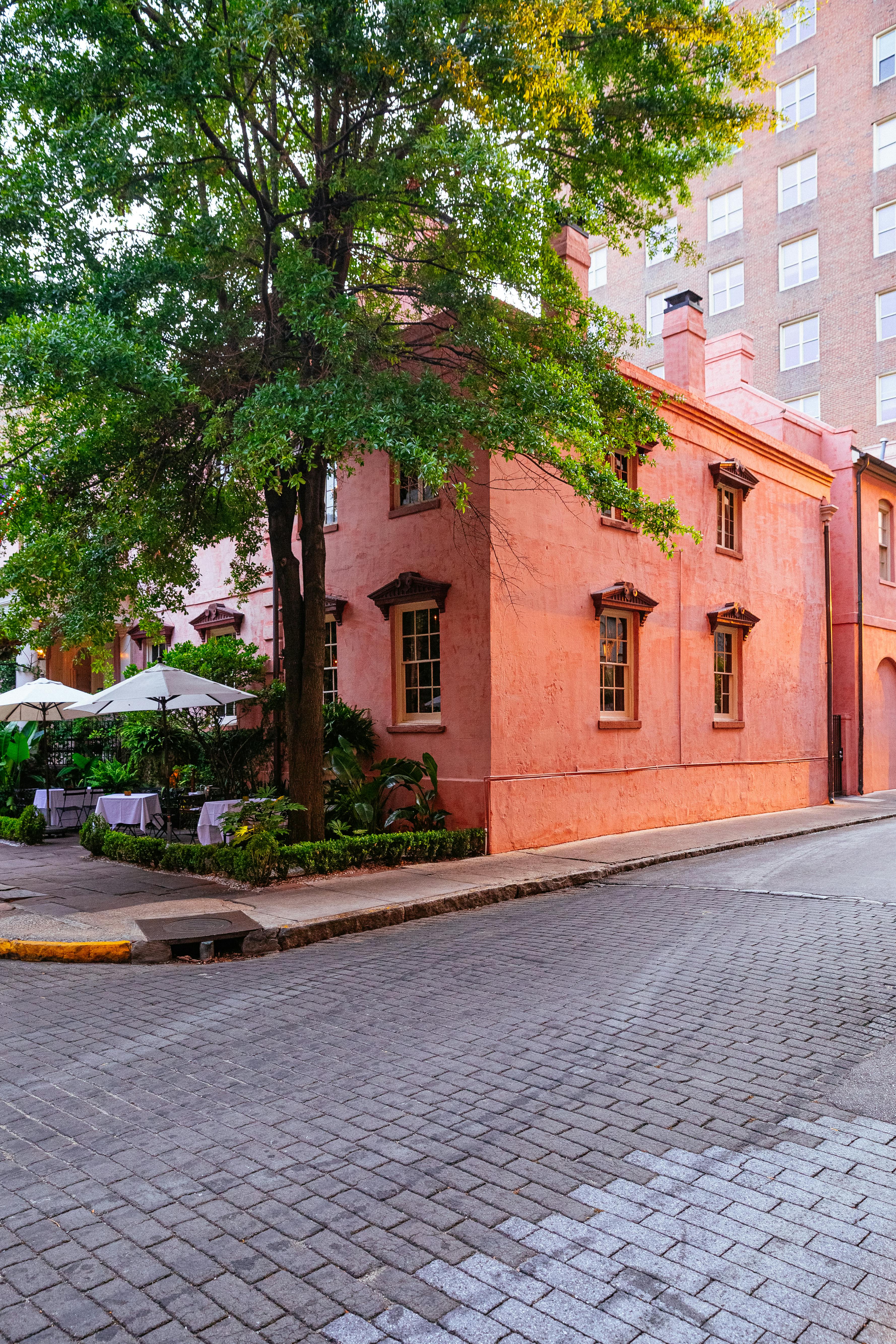 Corner view of a quaint pink building with lush trees in Savannah, GA.