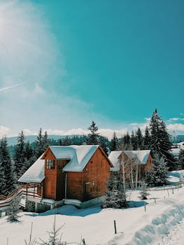 白雪覆盖的树木和湛蓝天空下的山脉，环绕着风景如画的木屋