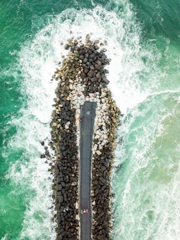 High-altitude shot of a stone breakwater surrounded by vibrant ocean waves.