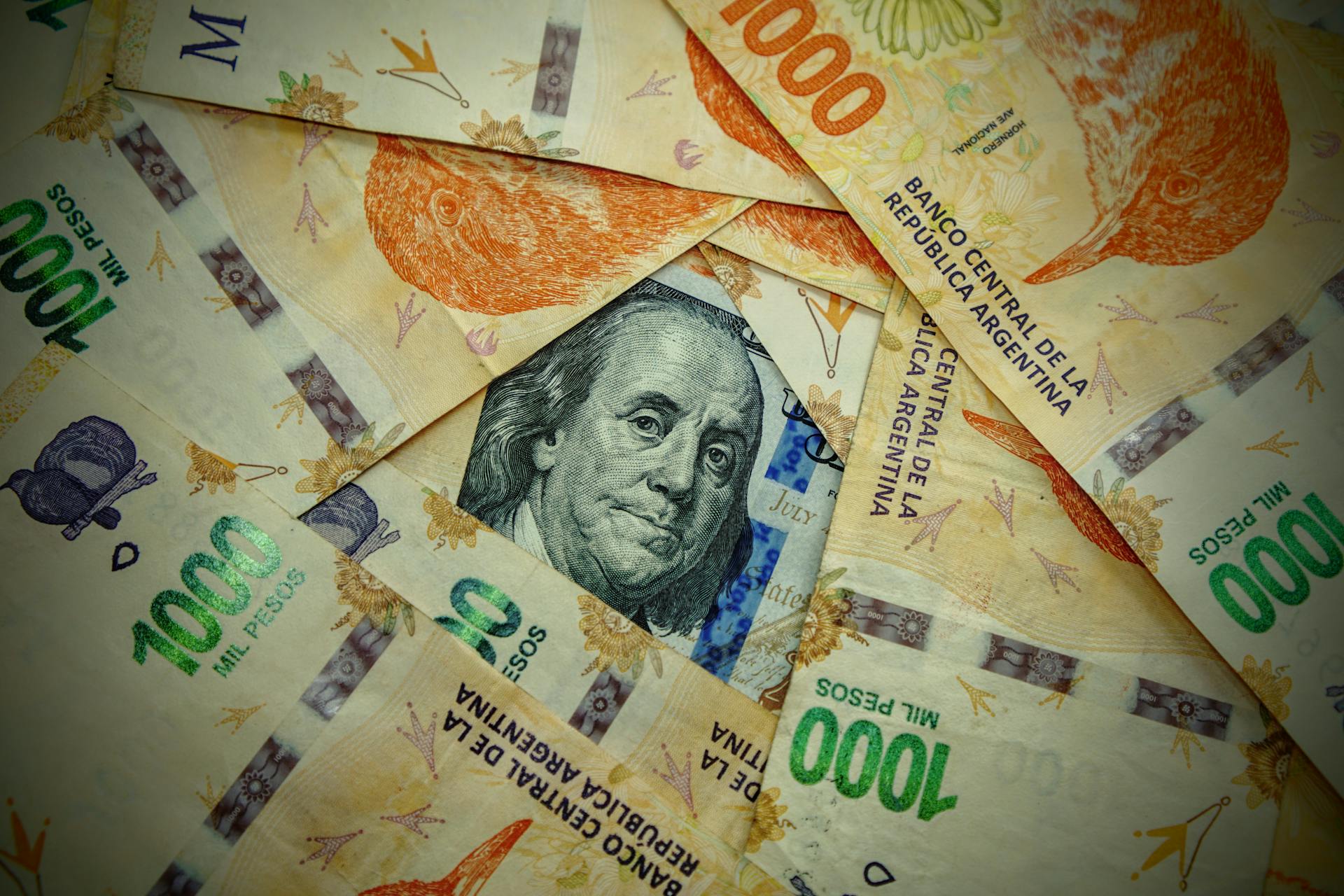 A detailed close-up of Argentinian pesos and a US dollar, showcasing currency contrast.