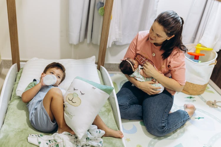 Mother Breastfeeding Baby Near Son On Bed