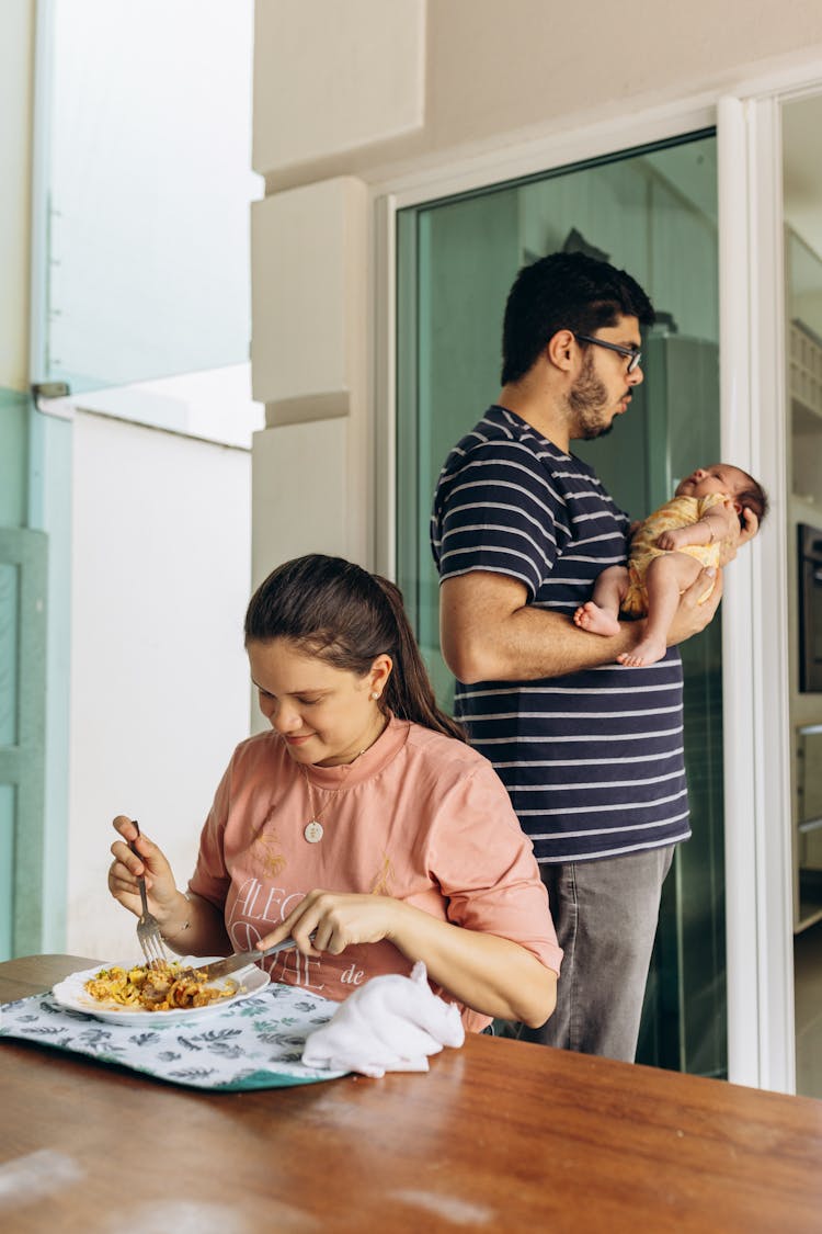 Man Holding Baby While Woman Is Eating Dinner