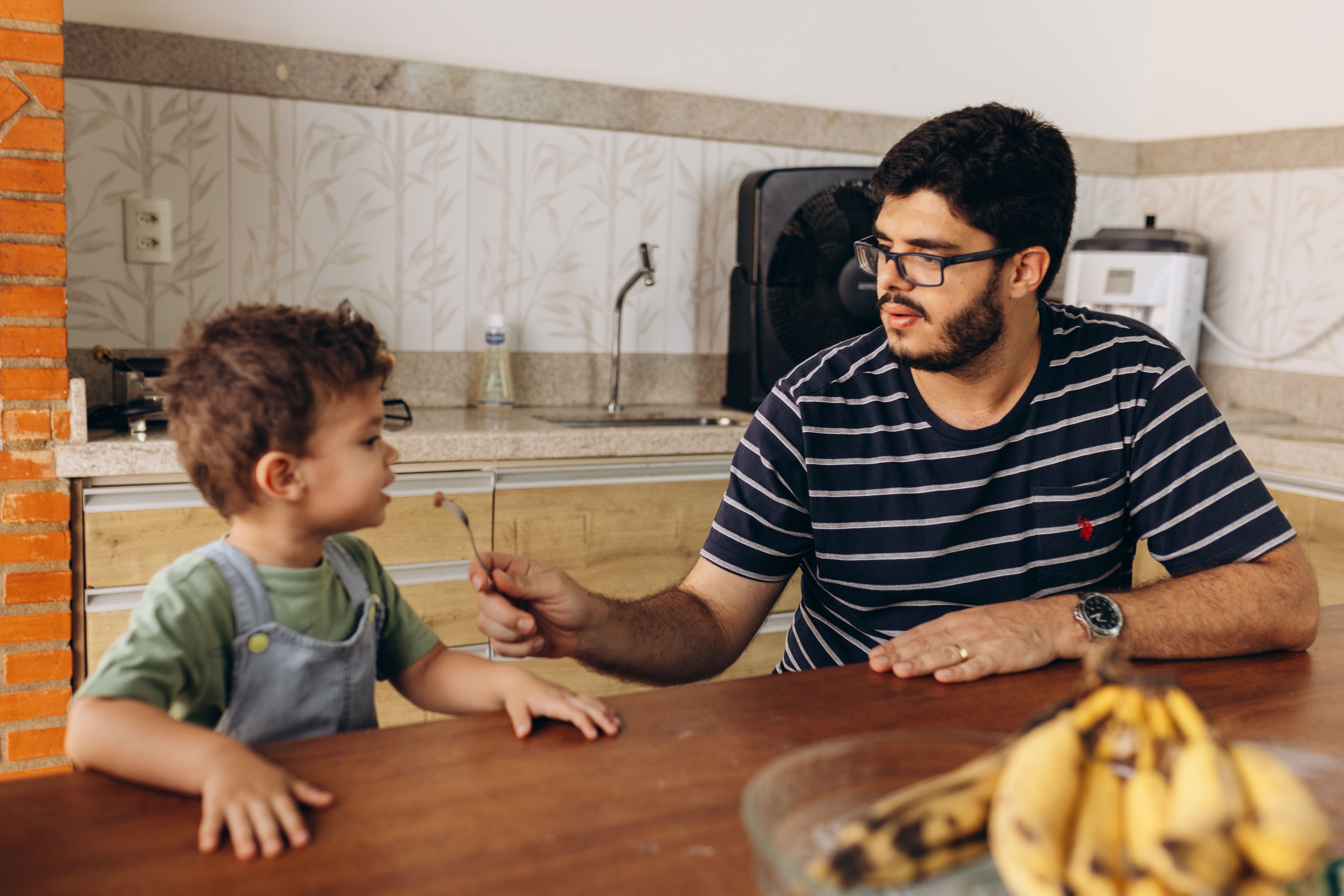 A father feeds his young son breakfast at the kitchen table in a cozy interior setting. - Photo by Jonathan Borba on Pexels