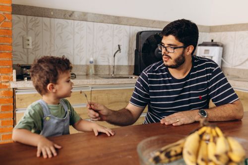 Free A father feeds his young son breakfast at the kitchen table in a cozy interior setting. Stock Photo