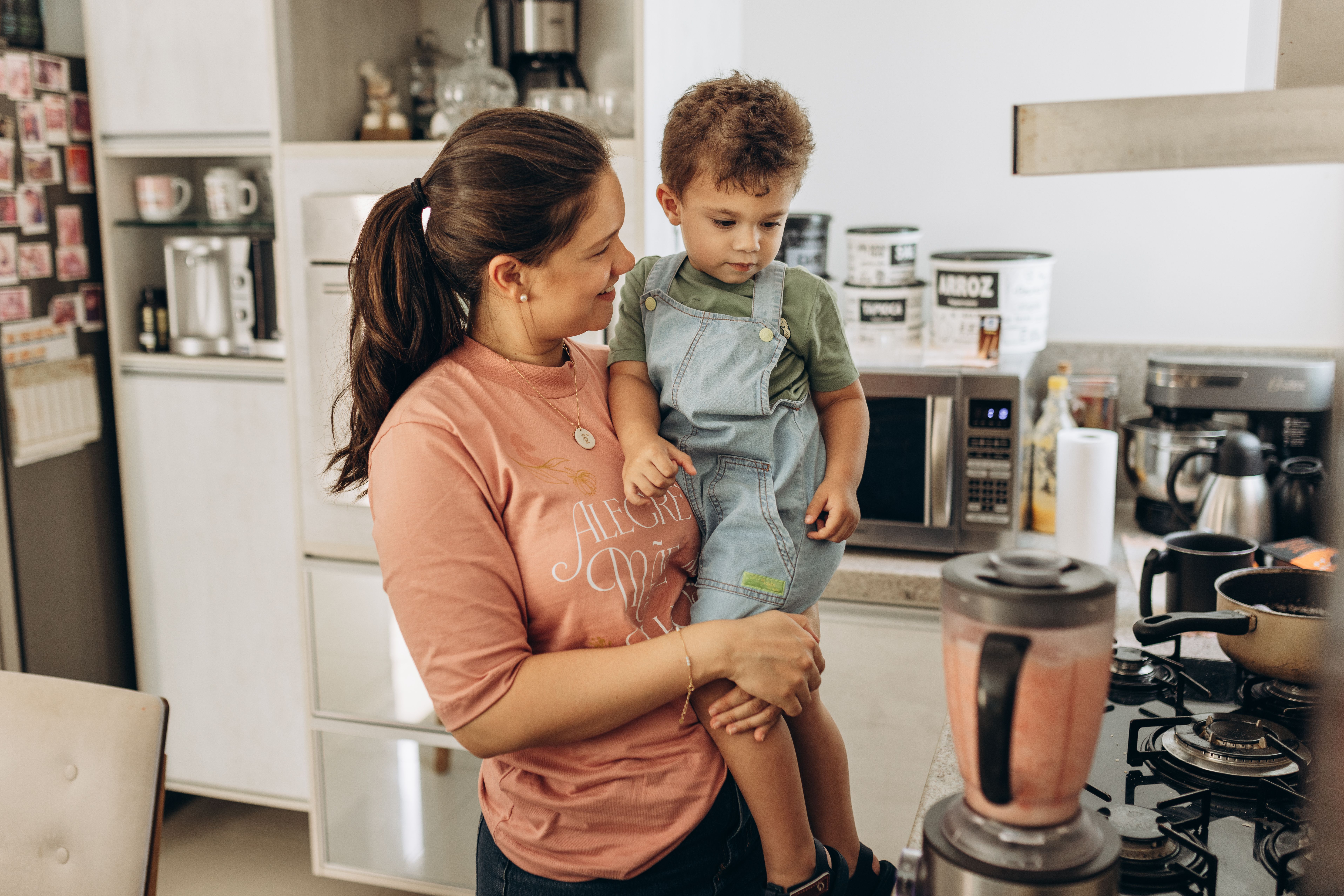 A mother holds her child in the kitchen while preparing food, creating a warm family moment.