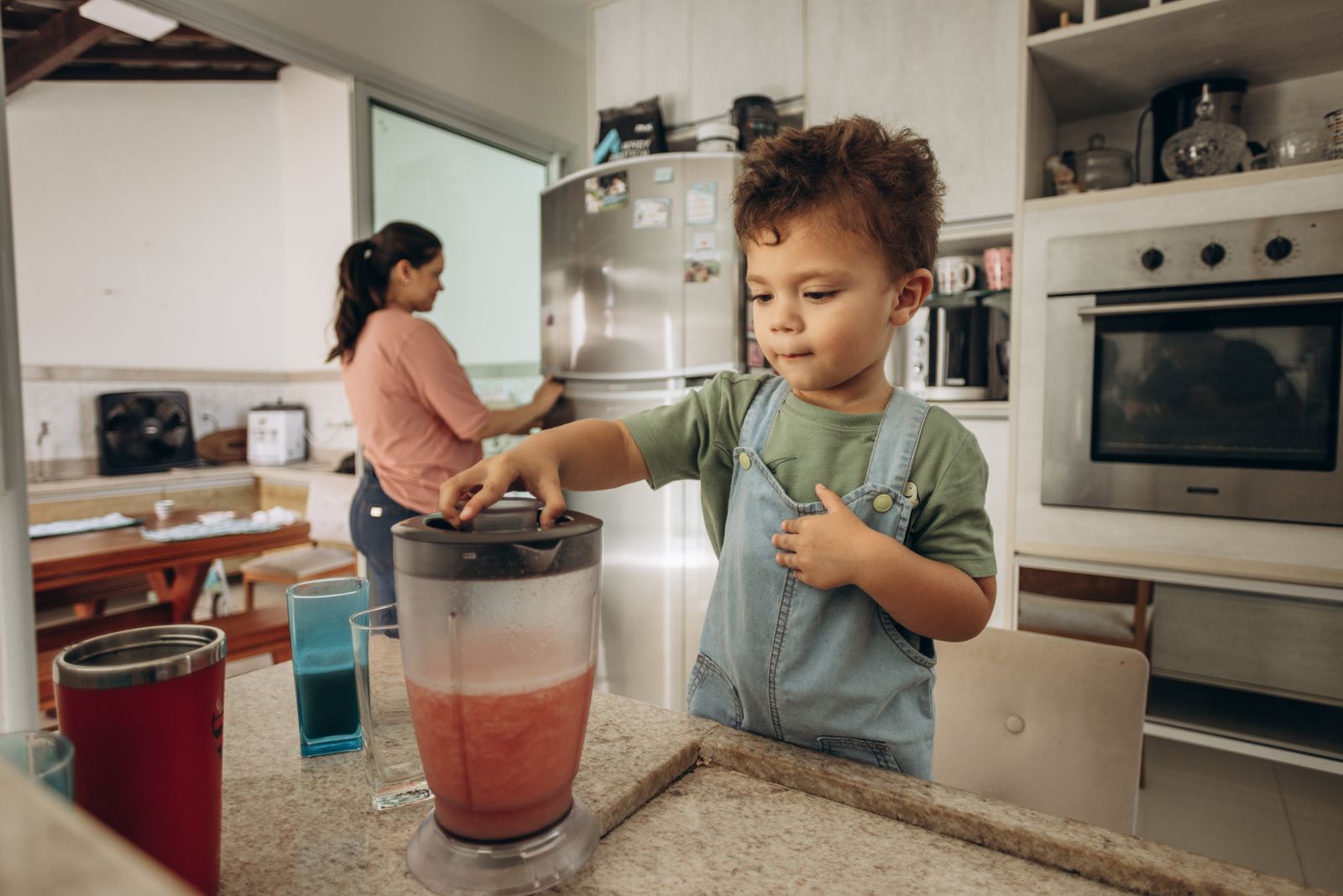 Parent and child preparing a smoothie with a blender in a modern kitchen