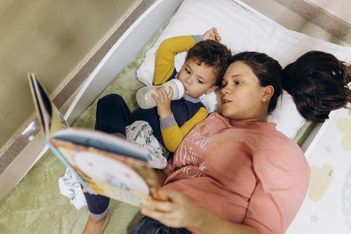 Free A mother and her young son reading a book together in bed, fostering a bond through storytelling. Stock Photo