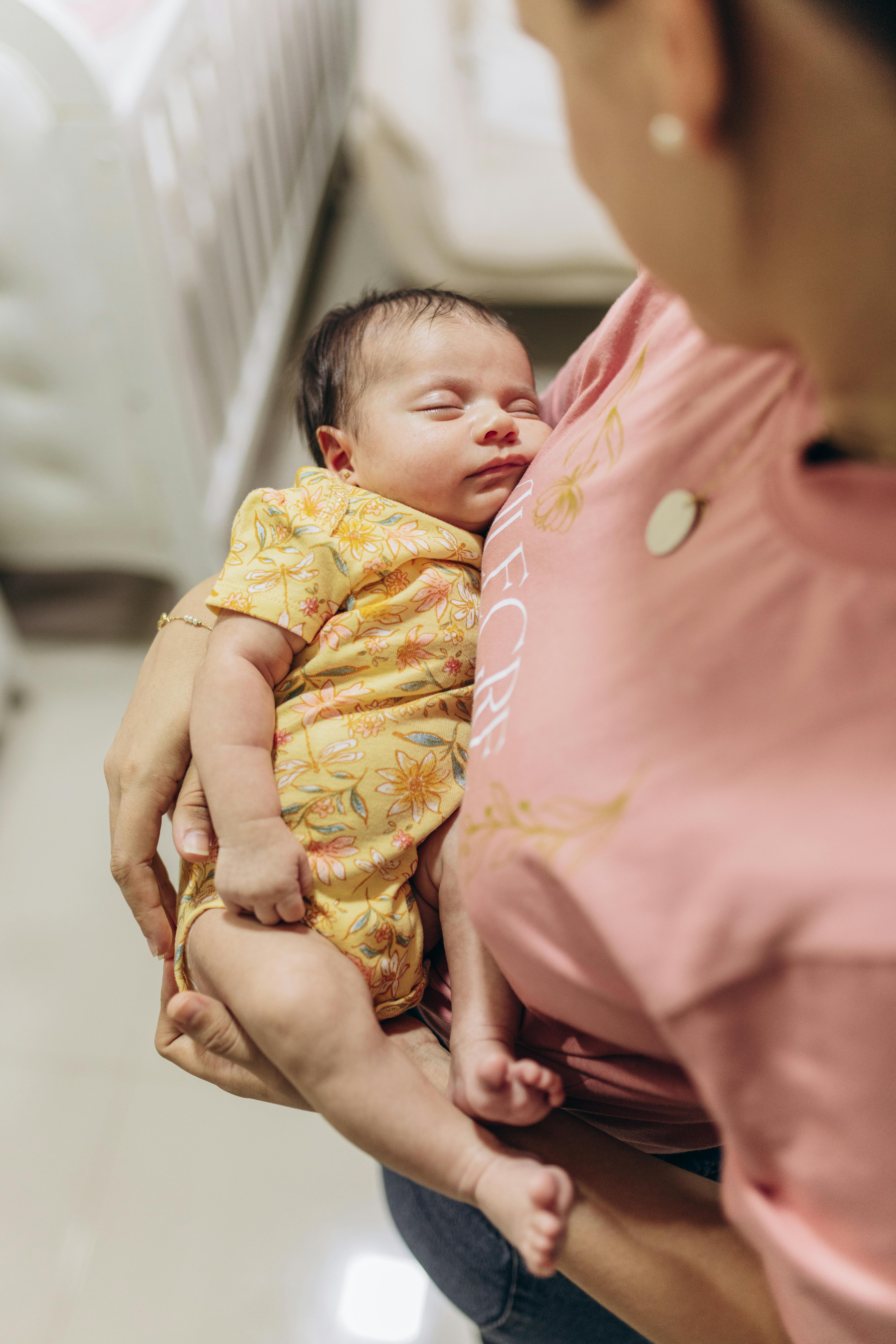 A tender moment of a mother holding her sleeping baby in a cozy indoor setting. Warm and intimate.