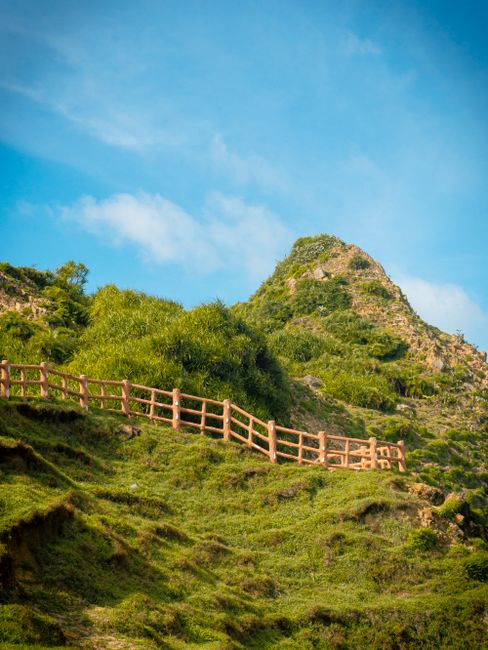 Beautiful rural scenery with a wooden fence and lush green hill under a clear blue sky.