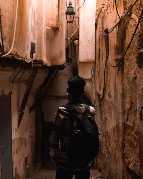 Free A man with a backpack walking through a narrow, historic alleyway. Stock Photo