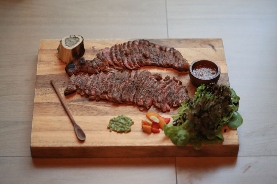 Sliced grilled skirt steak fanned out on a wooden cutting board, showing a charred crust and pink interior, with lime wedges and chopped cilantro alongside.