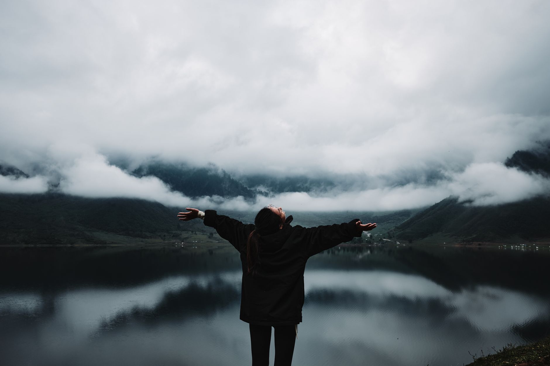 A person enjoys a sense of freedom by a misty mountain lake, embracing nature's tranquility.