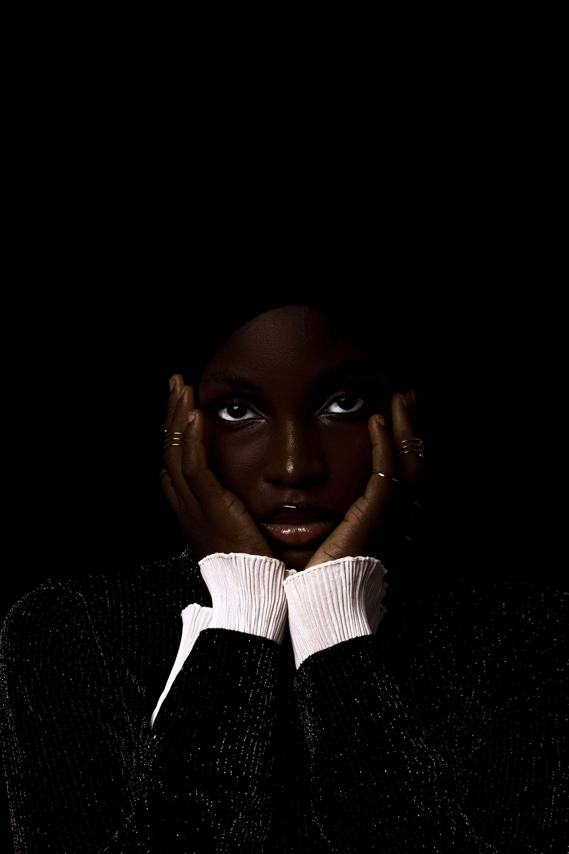 Moody portrait of a woman in low light with hands framing face elegantly.