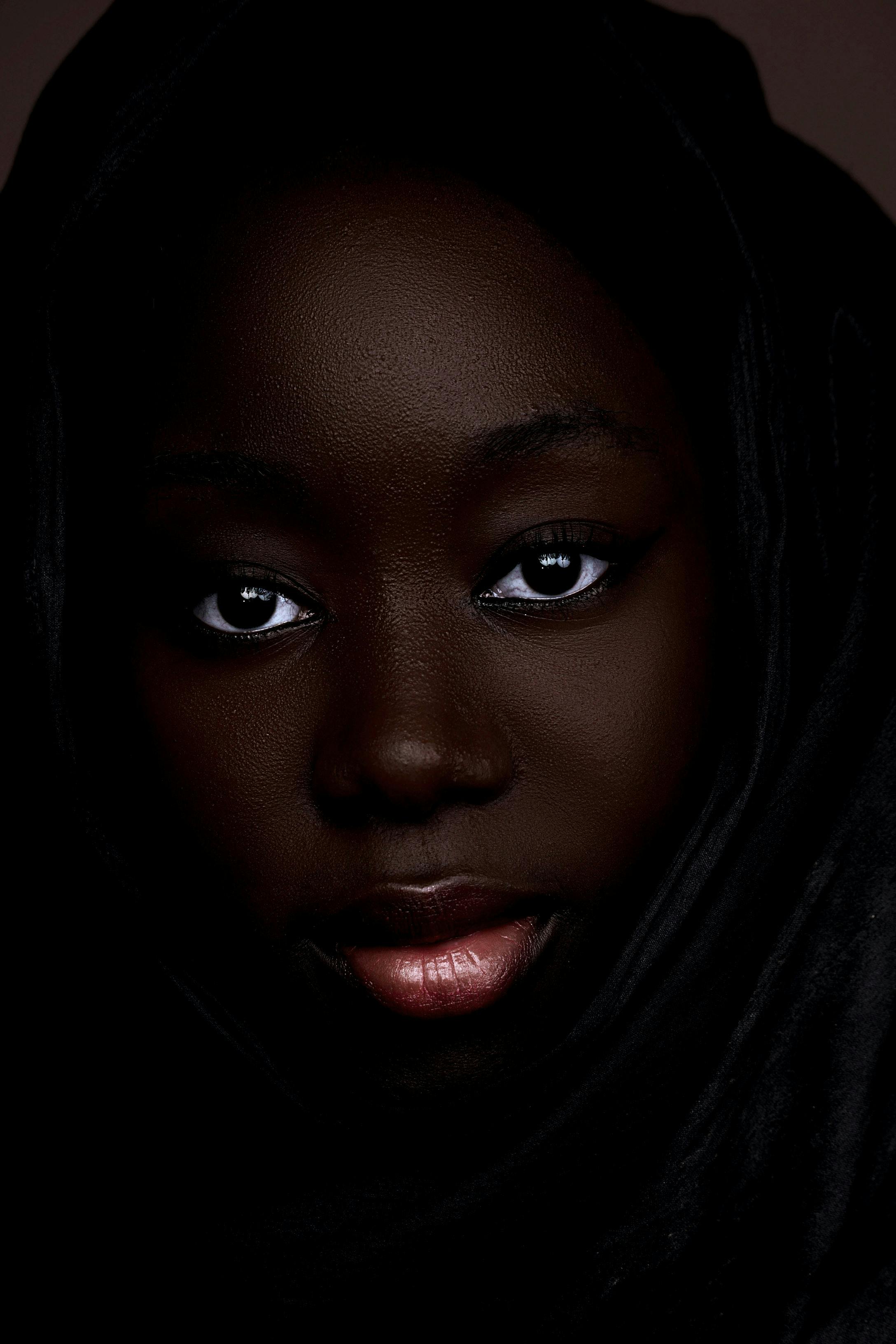 Close-up portrait of a woman with a headscarf in a dark studio setting.