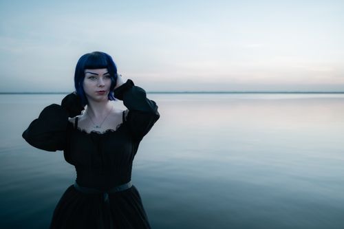 Free A tranquil portrait of a woman in black on a calm seashore during twilight, embodying elegance and peace. Stock Photo