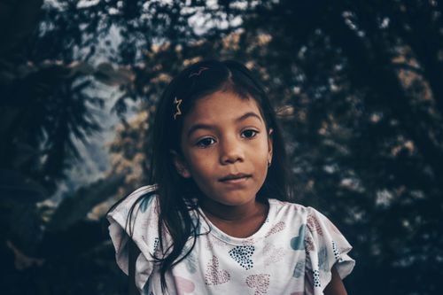 Free Portrait of a young girl with long hair outdoors surrounded by trees, exuding innocence. Stock Photo