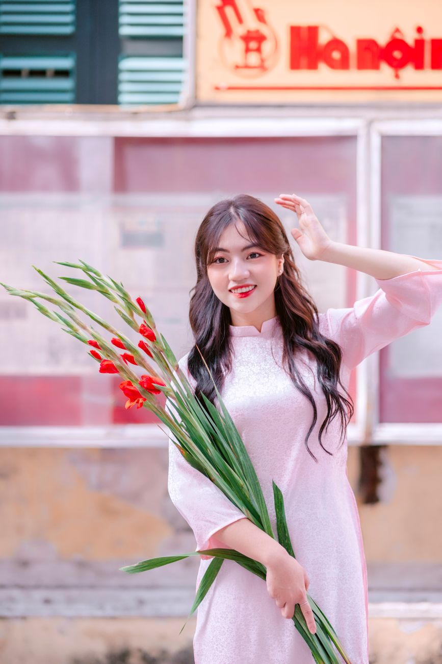 Portrait of a woman in a pink dress holding flowers, set against an urban backdrop.