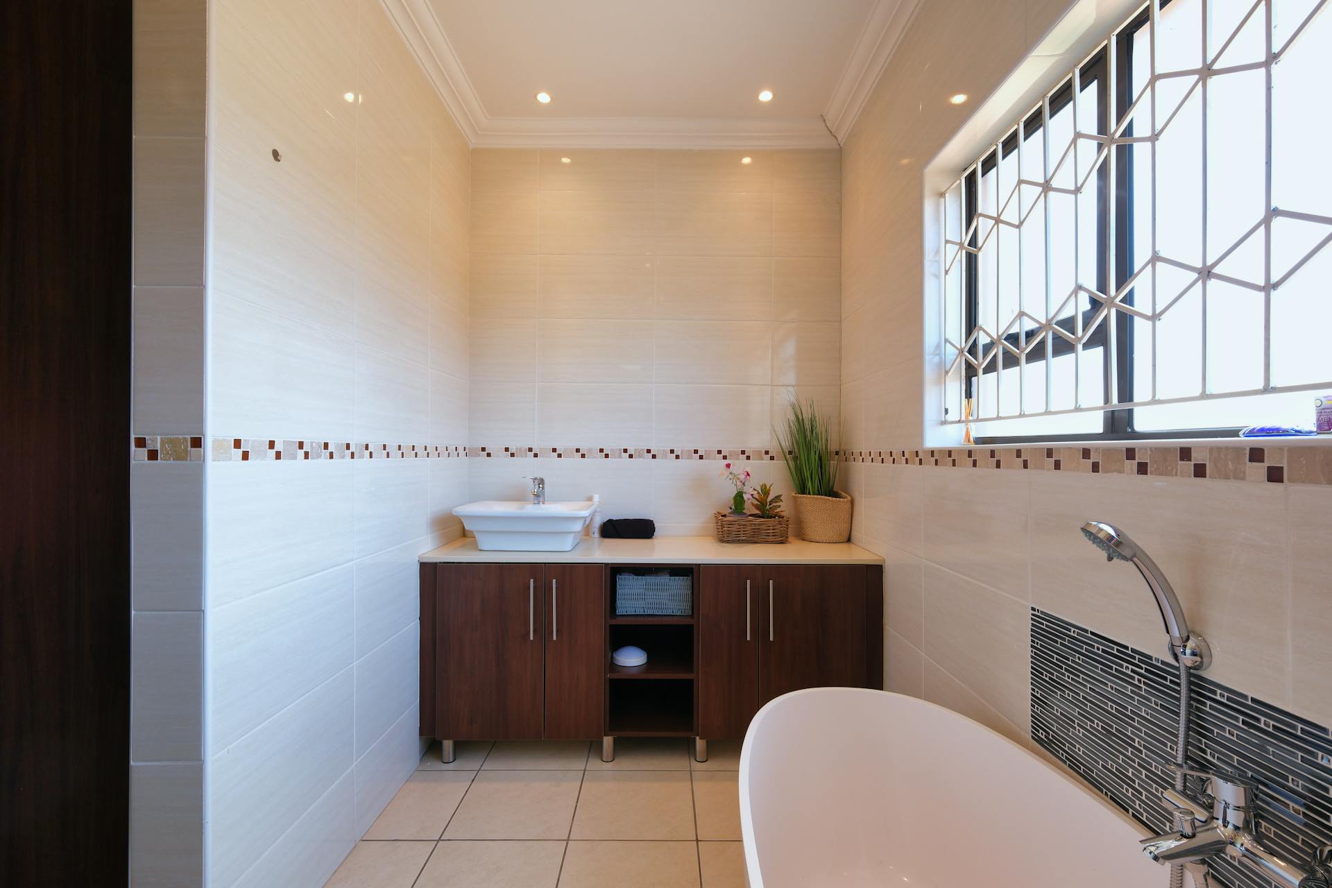 A spacious modern bathroom with beige tiles, wooden cabinet, and bathtub. Perfect for home interiors.