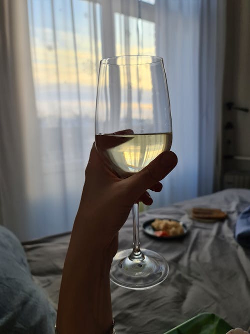 Close-up of a Person Holding a Glass of White Wine in Bed 