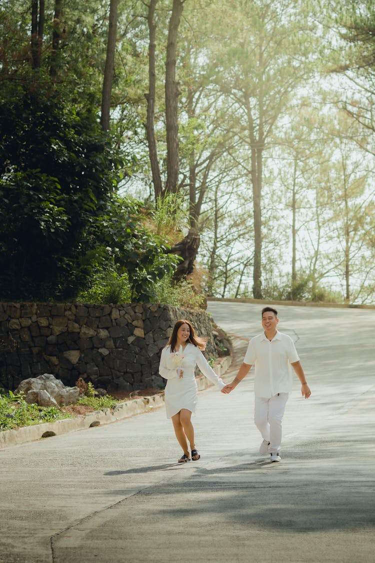 A Couple Walking On The Road Between Trees And Holding Hands