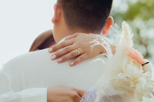 A romantic close-up of a couple embracing, highlighting the engagement ring and bouquet.