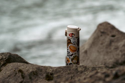 Water Bottle Decorated with Stickers on the Rocky Seashore