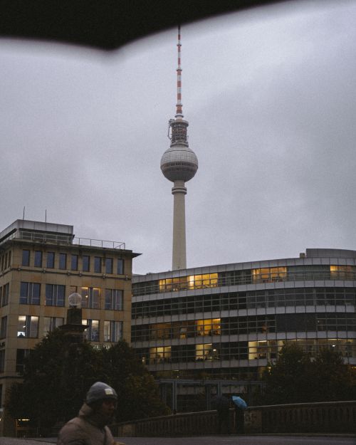 Free The Berliner Fernsehturm Tower rises amidst urban architecture in Berlin with a cloudy sky backdrop. Stock Photo