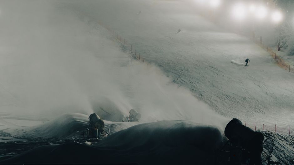 Skier on a snowy slope at night with lit snow cannons and a wintery atmosphere.