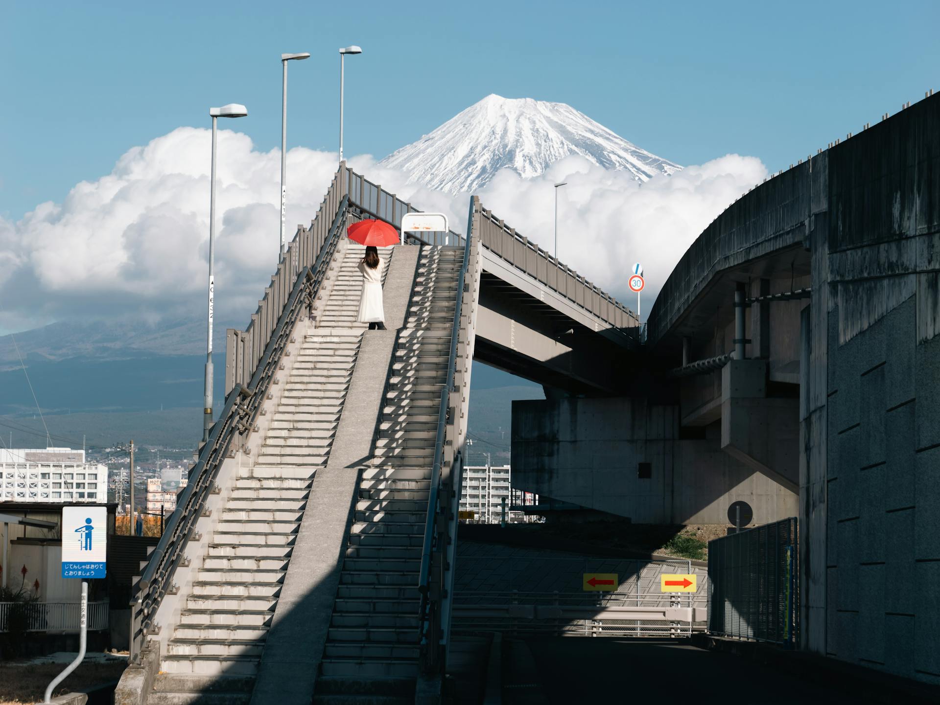 Woman Holding a Red Umbrella Standing on Steps of an Elevated Walkway with Mount Fuji in the Background