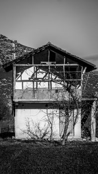 A monochrome image of an abandoned house in Çeltikçi, Türkiye, set against mountain scenery.