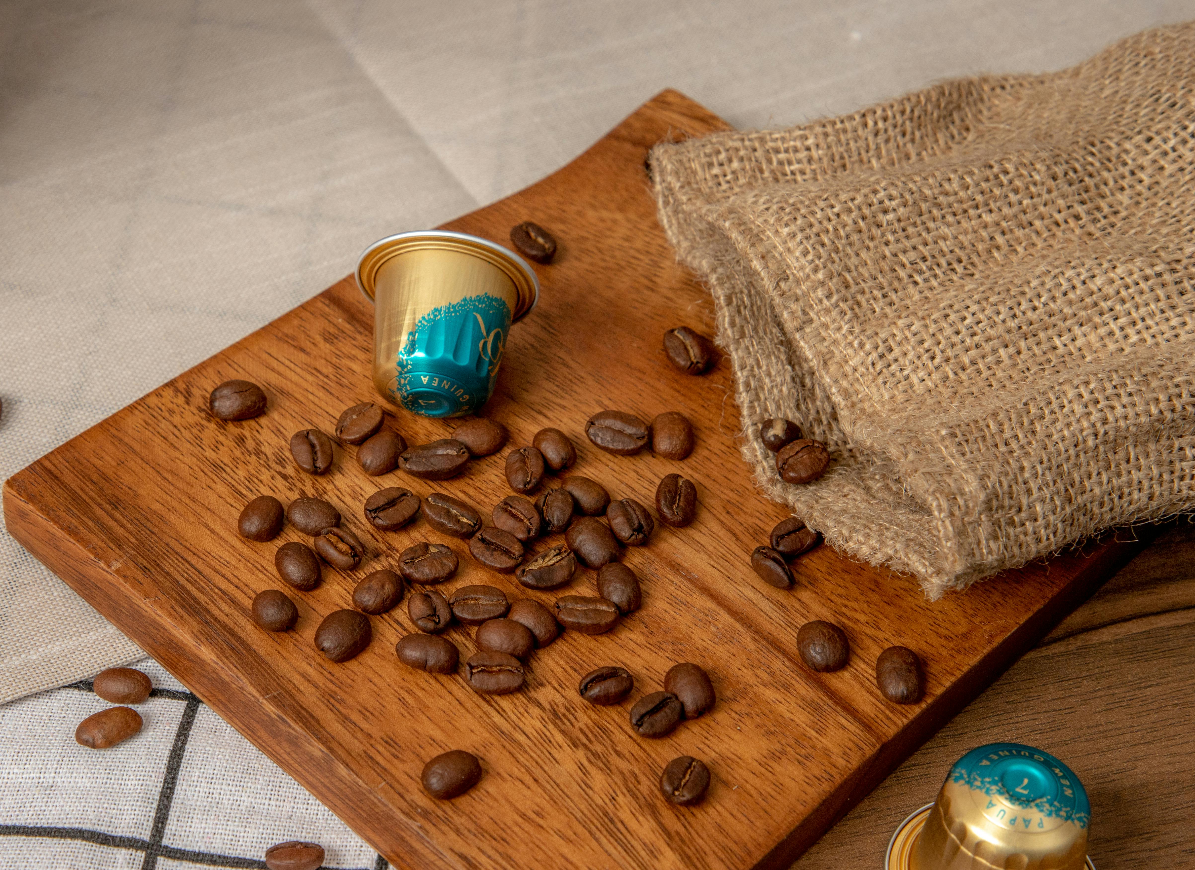 Grains de café torréfiés et capsules sur une planche en bois avec sac en toile de jute