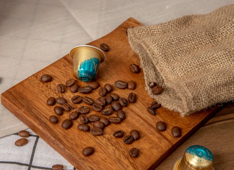 Roasted coffee beans and capsules on a wooden cutting board with a burlap sack, evoking a warm and rustic feel.